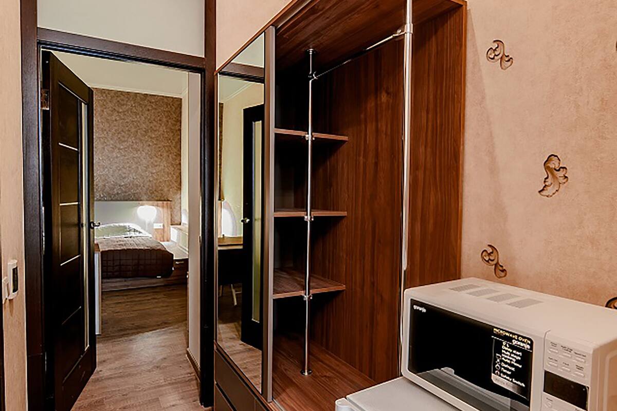 A hotel room with a wooden floor, a wardrobe, a mirror, and a microwave.