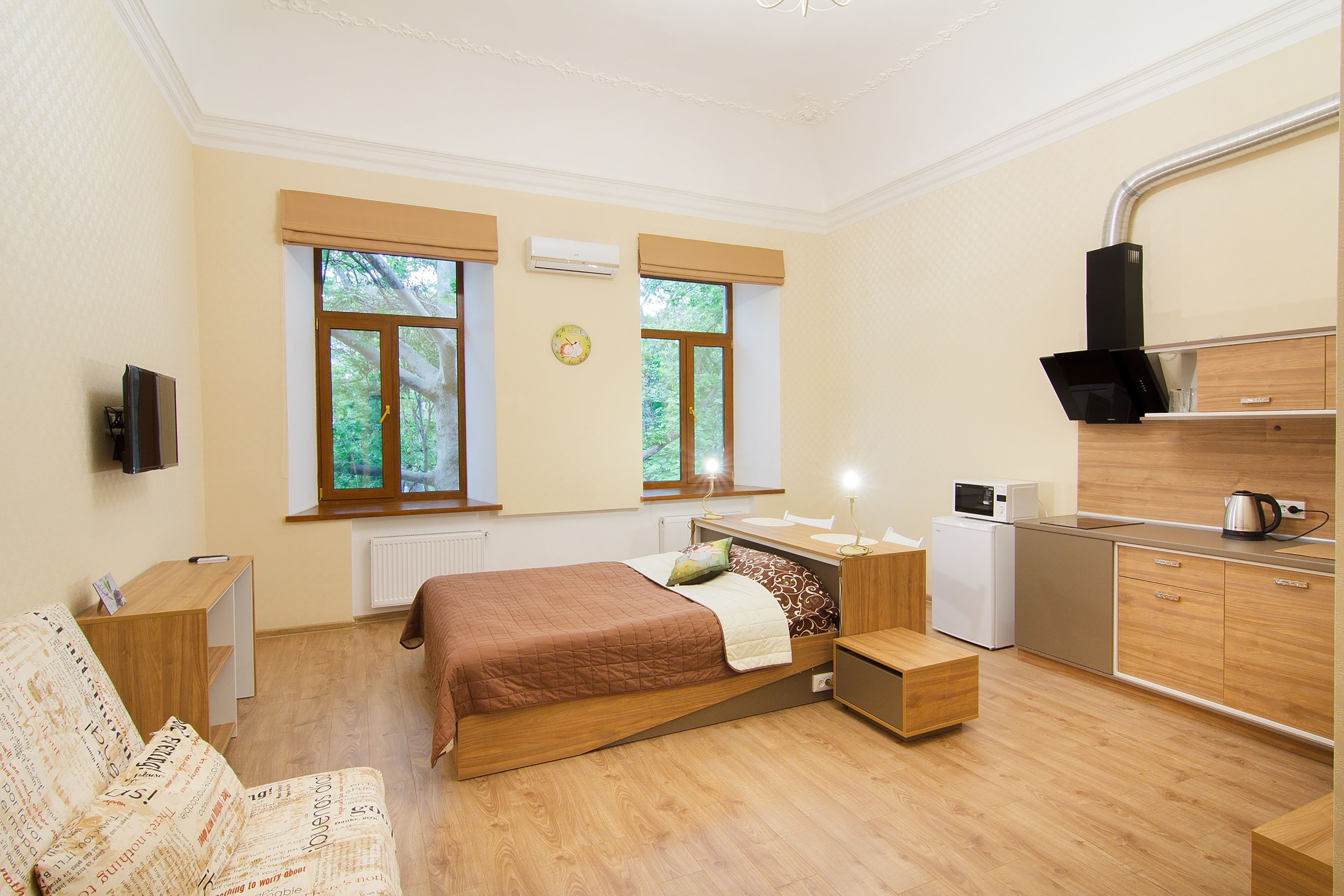 A bedroom with a bed, bedside table, TV, and a kitchenette with a microwave and kettle.