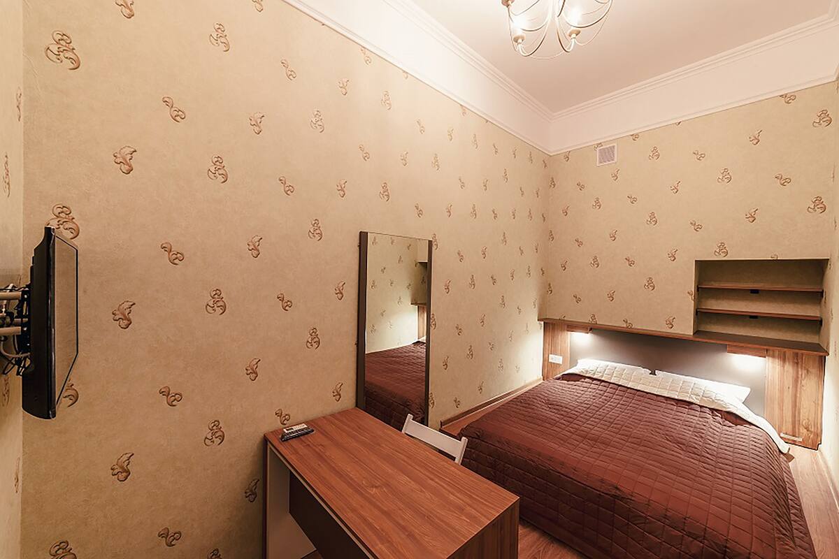 A hotel room with a bed, a desk, a mirror, and a TV.