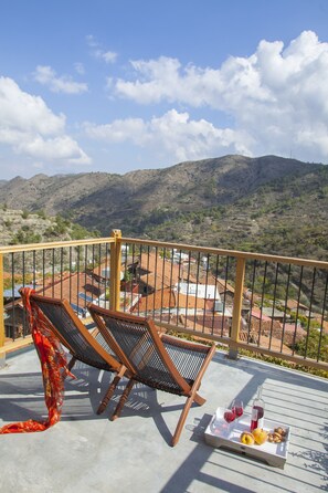 A balcony with two wooden lounge chairs, a tray with wine glasses, a bottle, fruit, and nuts. - Lyhnos (Askas)