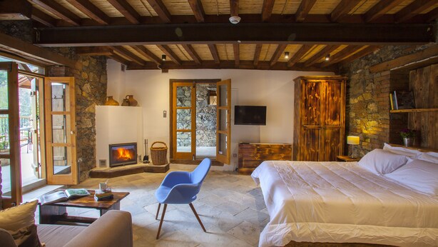 A cozy room with a stone fireplace, a bed, a blue chair, and a television. - Lyhnos (Askas)