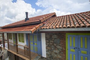 A building with a red-tiled roof, stone walls, and doors with green and blue shutters. - Lyhnos (Askas)