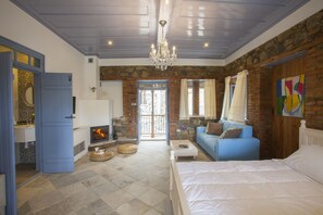 A bedroom with a large bed, a blue sofa, a fireplace, and a stone wall. - Lyhnos (Askas)