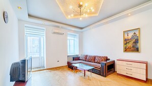 Ett vardagsrum med en soffa, ett soffbord i glas, en tv, ett element och en tavla på väggen.