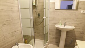 Un baño con cabina de ducha de vidrio, lavamanos sobrepedestal y retrete.