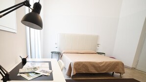 Un dormitorio con cama, escritorio con papeles, lámpara y ventana.