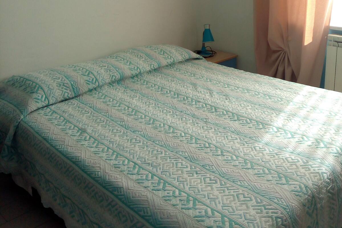 A bedroom with a bed, a nightstand, a lamp, and a painting on the wall.