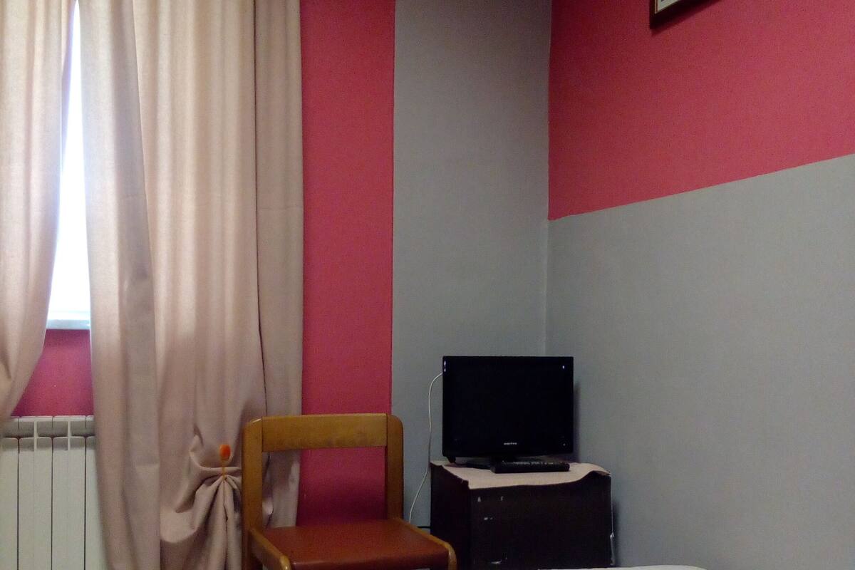 A bedroom with a bed, a chair, a television, and a radiator.