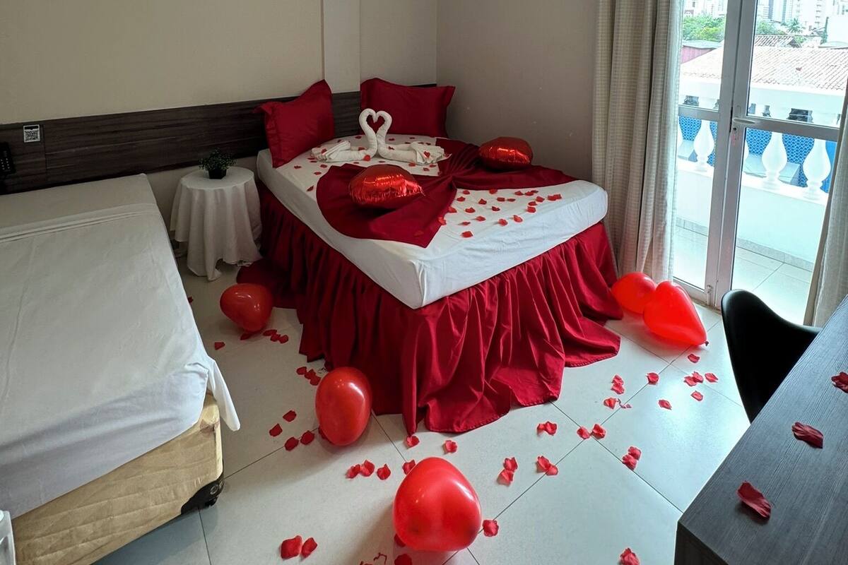 A hotel room with a bed, a bedside table, and a view of the outside.