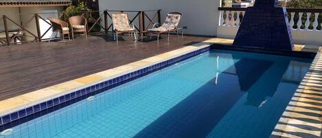 A rooftop pool with tiled blue water, surrounded by lounge chairs and a cityscape view.