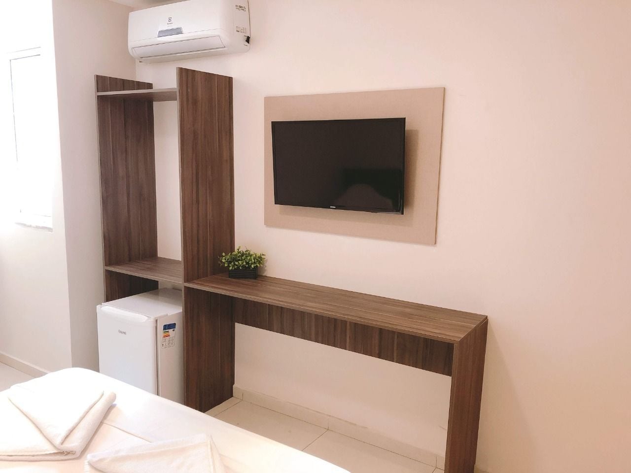 Una habitación moderna con televisión integrada, un refrigerador pequeño y un mueble de madera.