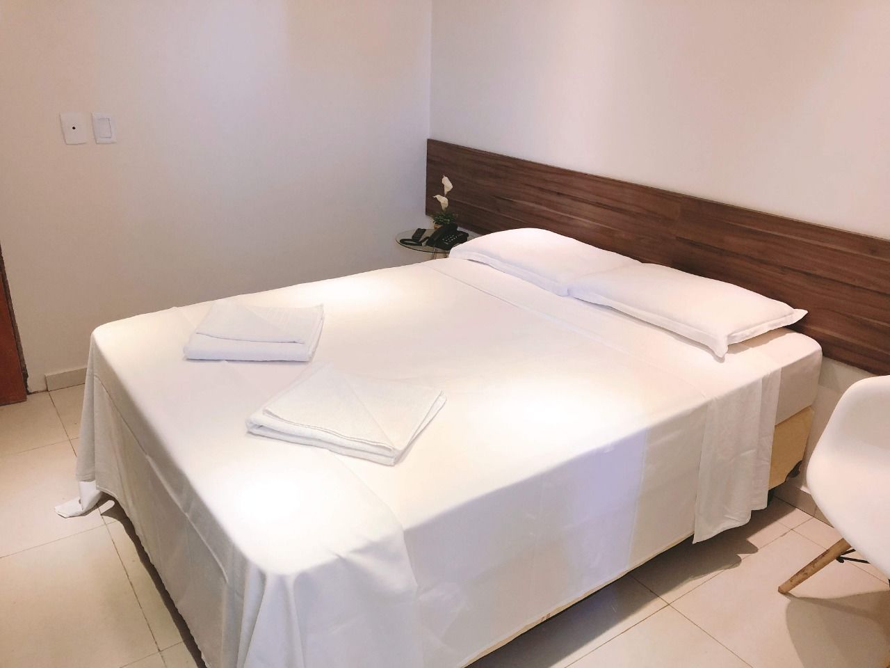 Una cama bien hecha con sábanas blancas y una toalla doblada al lado.