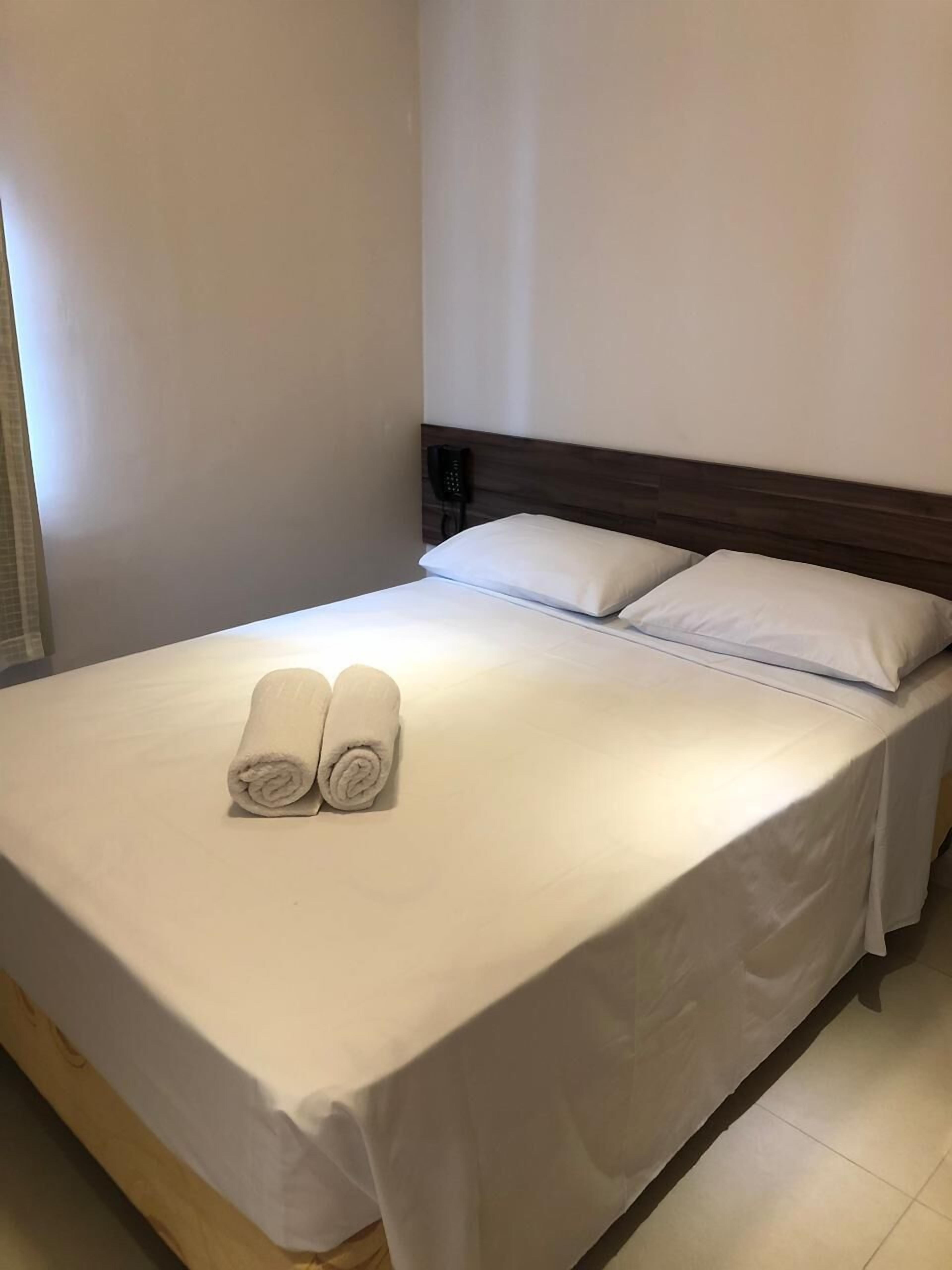 A neatly made bed with two rolled towels and a wooden headboard in a hotel room.