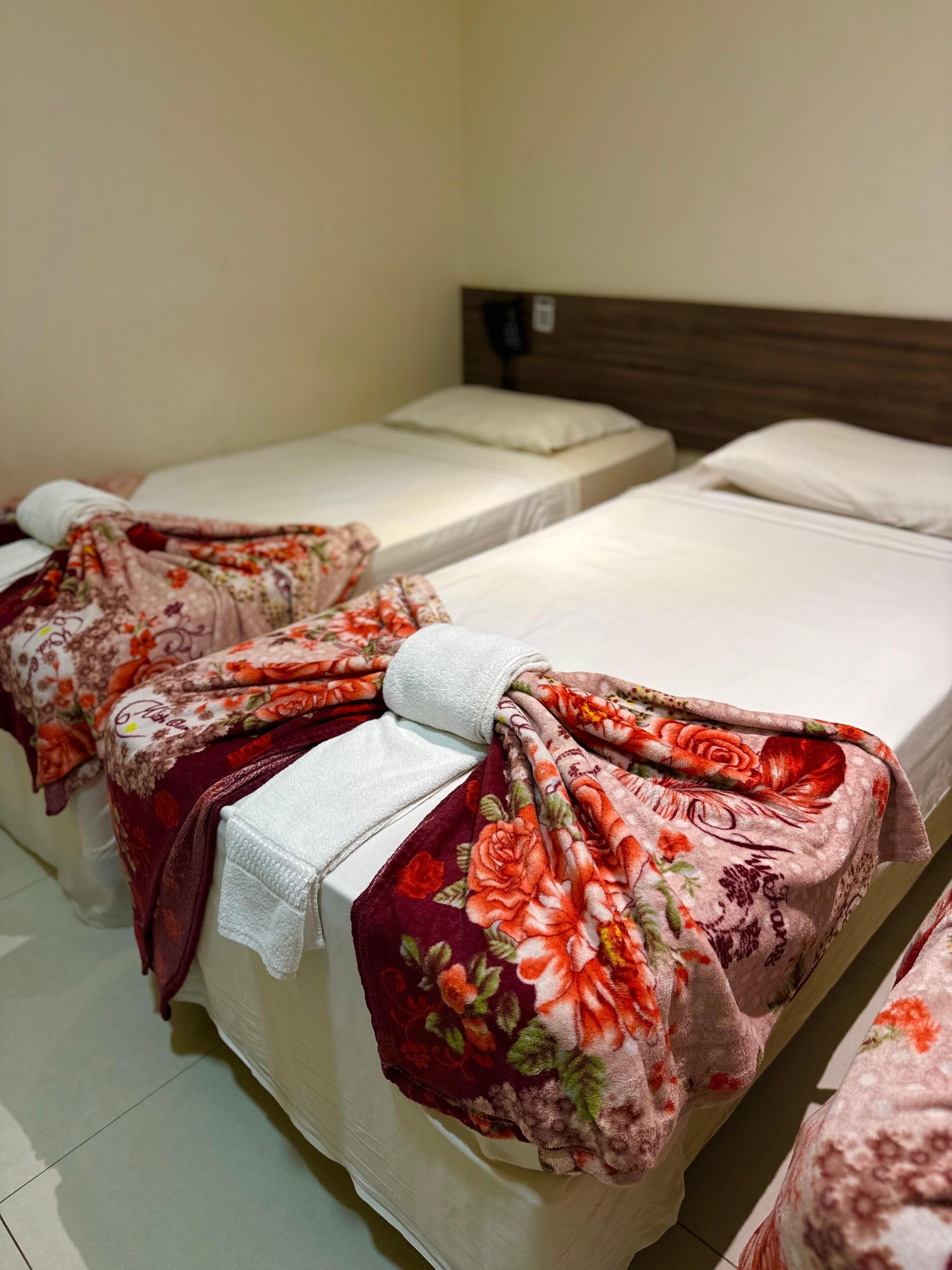 A hotel room with two beds, each covered with floral-patterned blankets and white sheets.
