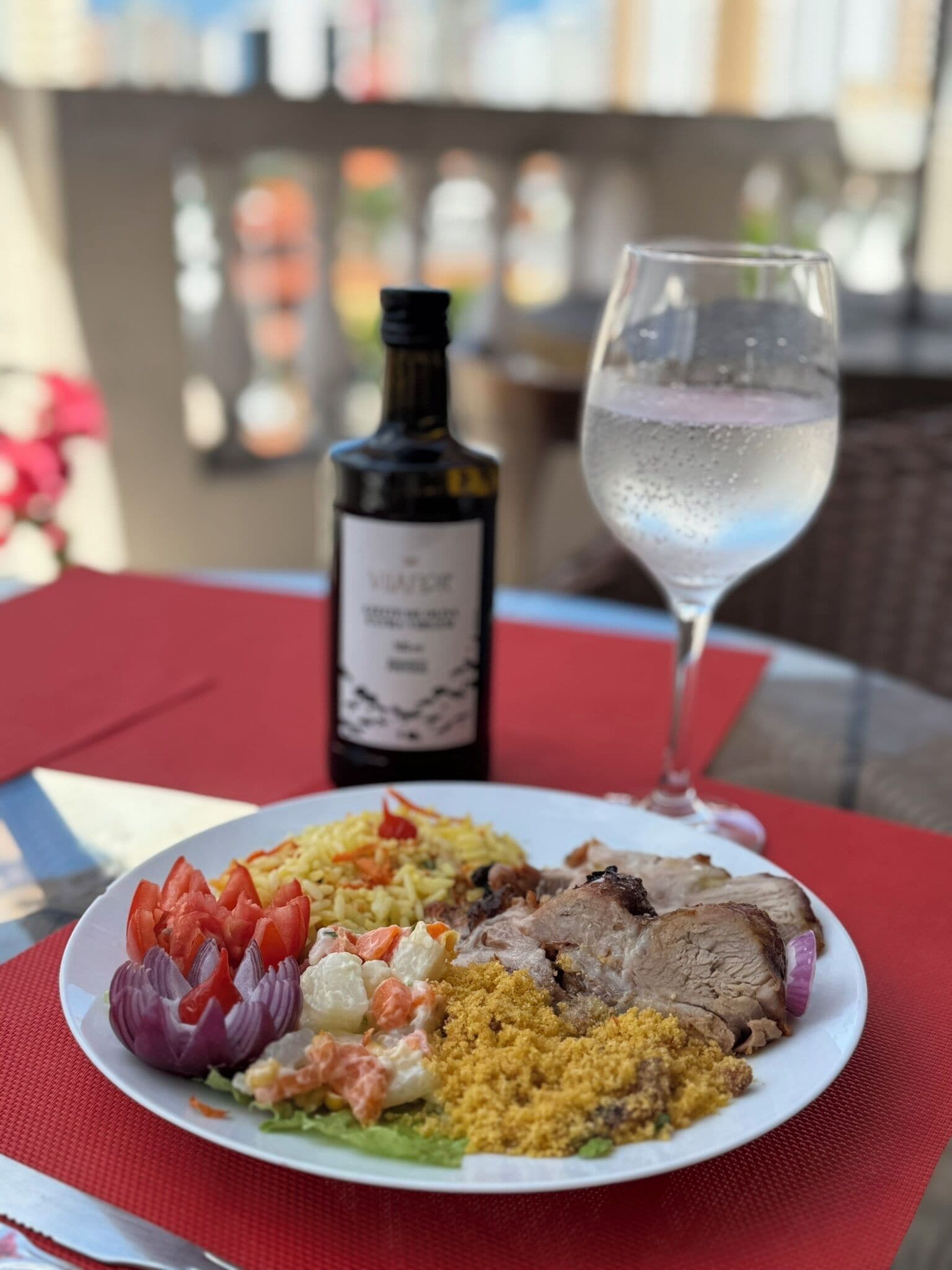 A plate of food with a bottle of wine and a glass of water on a red tablecloth.