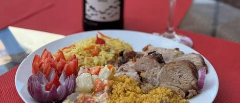 Un plato de comida con una botella de vino y un vaso de agua sobre un mantel rojo.