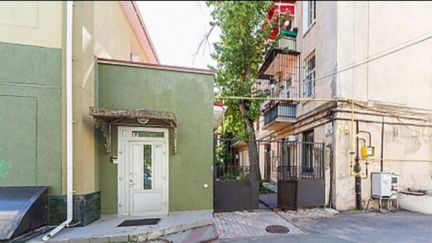 A narrow street with a green building on the left, a white door, and a metal gate. - Apartment Sea and City Center (Odesa)