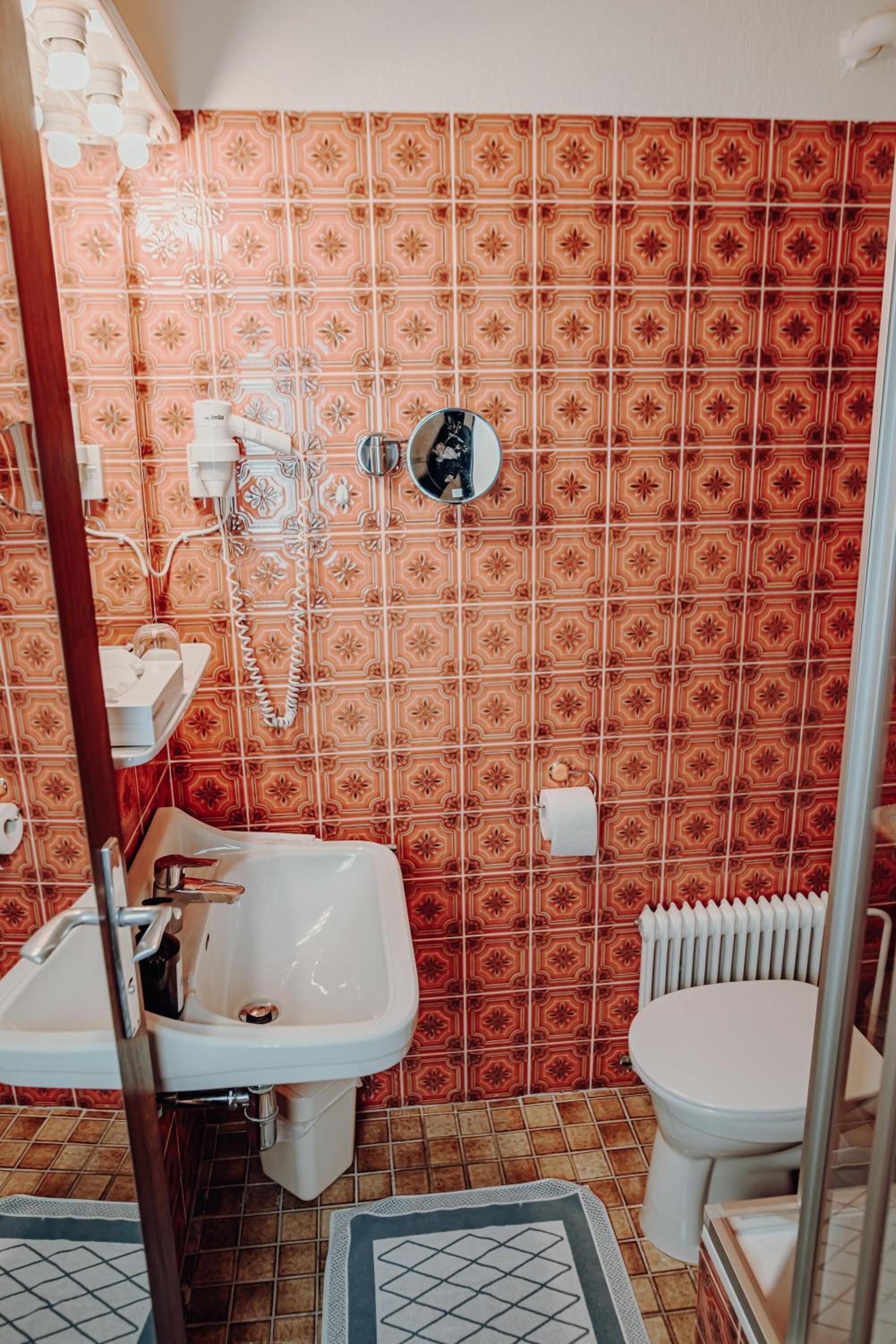 A bathroom with a patterned tile wall, a white sink, a toilet, and a shower area.