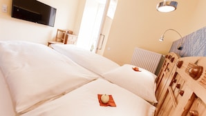 A hotel room with two beds, a TV mounted on the wall, a wooden headboard, and a window with a view.