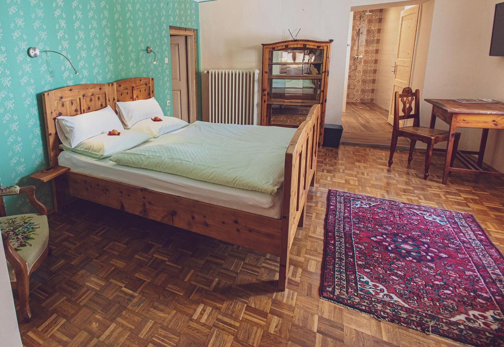 Una habitación con cama de madera, un escritorio de madera, una silla, un radiador y una alfombra estampada.