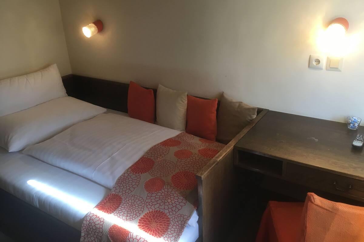 A hotel room with a bed, a bedside table, a lamp, and a wall-mounted light fixture.