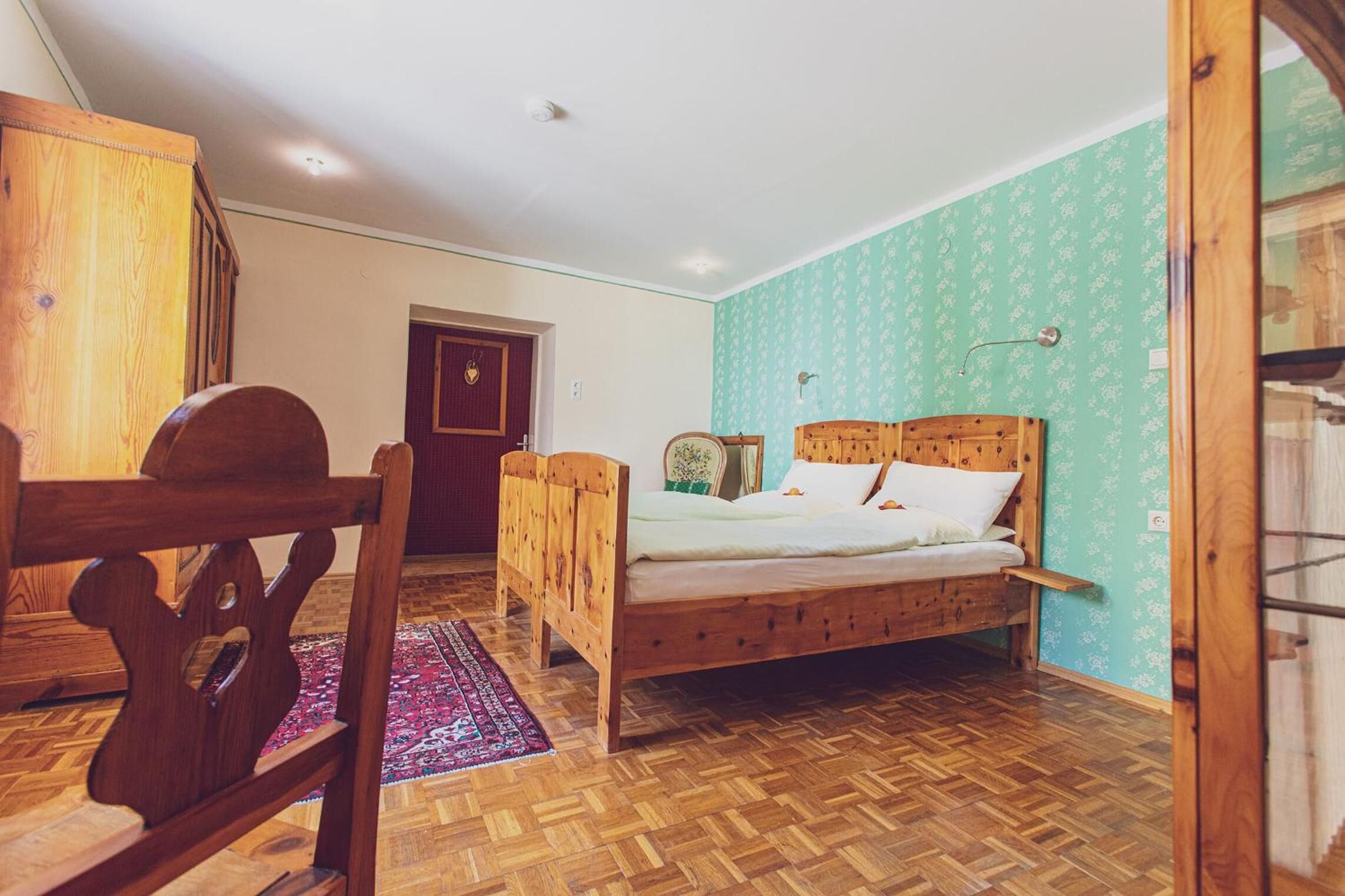 A bedroom with a wooden bed, a wooden wardrobe, and a door leading to another room.