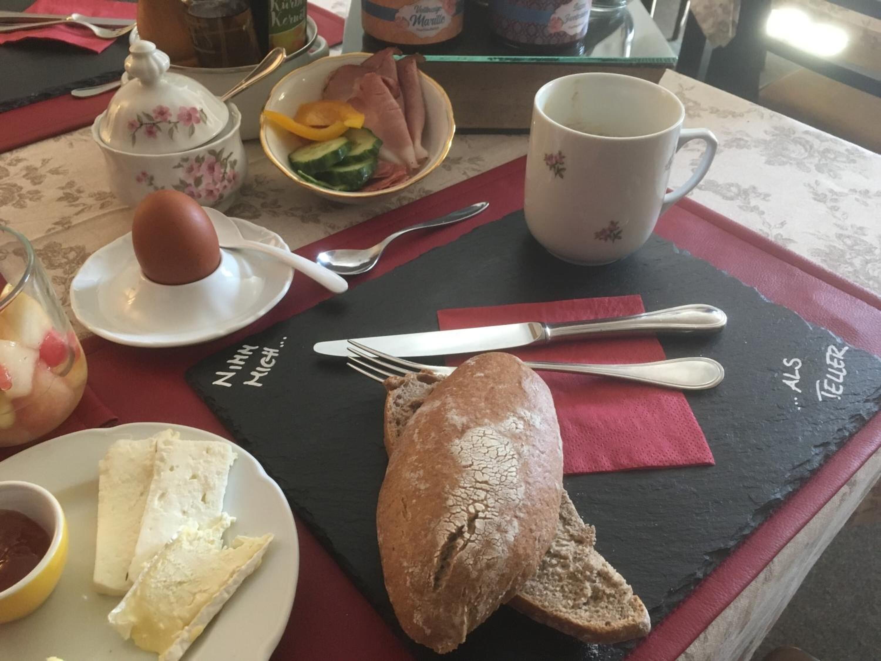 Impostazione per la colazione con un piatto di pane, una ciotola di frutta a fette, una tazza e un piccolo contenitore con un uovo sodo.