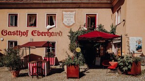 A building with a sign reading "Gasthof Eberhard" and a red awning over a table and chairs.