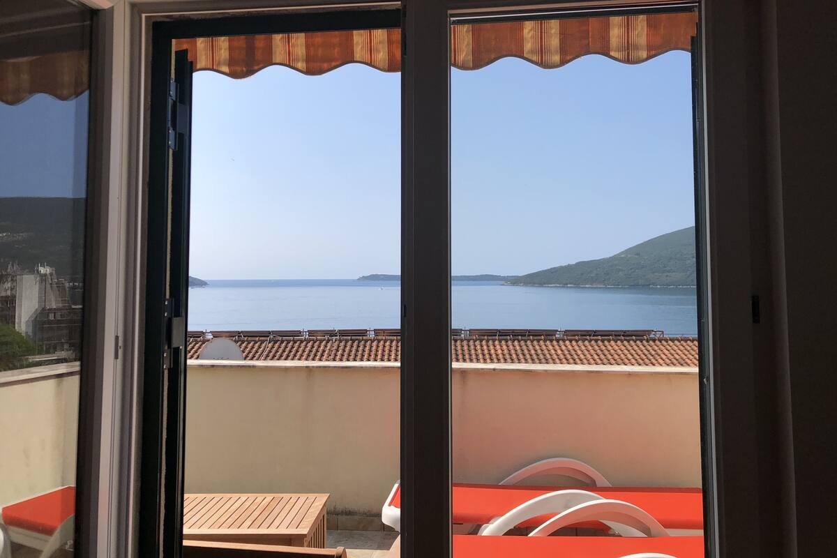 A balcony with a view of the sea, a wooden table, and a red chair.