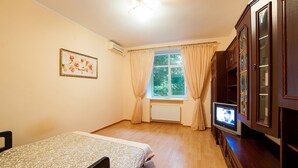 A bedroom with a bed, a television, a window with curtains, and a cabinet with glass doors. - Apartment City Center Osipova 4 (Odesa)