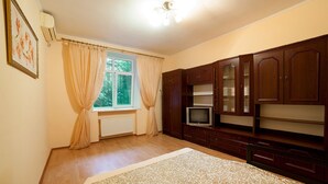 A bedroom with a bed, a television, wooden cabinets, a radiator, and a window with curtains. - Apartment City Center Osipova 4 (Odesa)