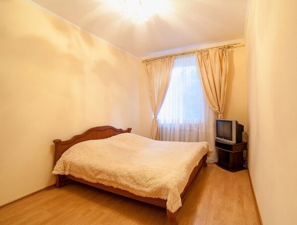 A bedroom with a wooden bed, a television on a stand, and a window with curtains.