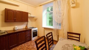 A small kitchen with wooden cabinets, a stove, and a window with curtains. - Apartment City Center Osipova 4 (Odesa)