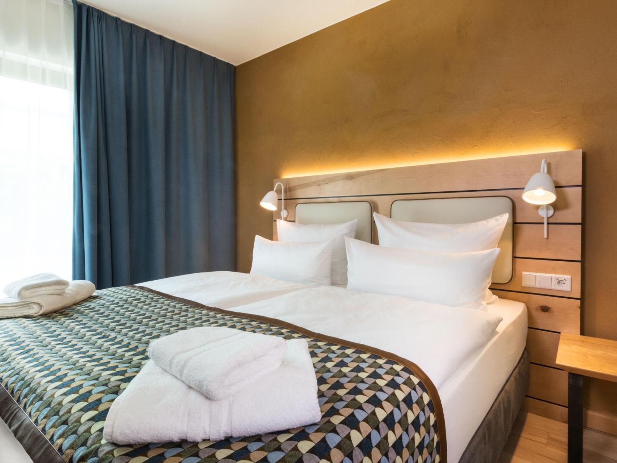 A hotel room with a large bed, two bedside lamps, a telephone, and a neatly folded towel on the bed.