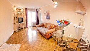 A cozy living room with a sofa, a glass table with chairs, a stone wall, and a TV. - Balcony Apartment near Deribasovskaya (Odesa)