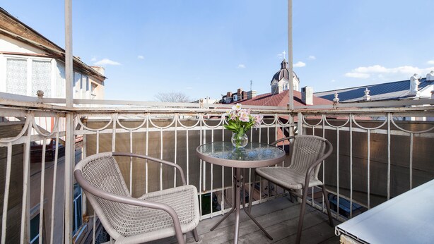 A balcony with wicker chairs, a glass table, and a vase with flowers. - Balcony Apartment near Deribasovskaya (Odesa)