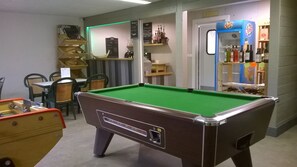 Ein Billardtisch in einem Raum mit Stühlen, einem kleinen Tisch mit einer Speisekarte und einem Regal mit Flaschen.