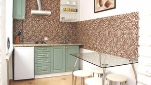 Uma cozinha compacta com armários verdes, uma geladeira branca, painel de azulejos e uma mesa de vidro com banquetas.