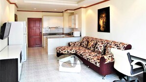 A compact living space with a sofa, a glass coffee table, a TV, a refrigerator, and a kitchen area with cabinets and a microwave. - Sea Views With Rentbuythailand (Pattaya)