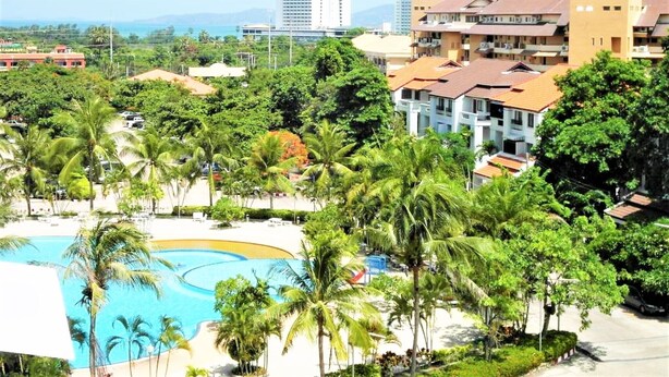 A resort with a swimming pool surrounded by palm trees, a beachfront, and modern buildings in the background. - Sea Views With Rentbuythailand (Pattaya)