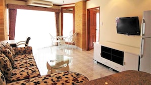 A living room with a sofa, a glass table, and chairs. There is a TV mounted on the wall and a refrigerator. - Sea Views With Rentbuythailand (Pattaya)