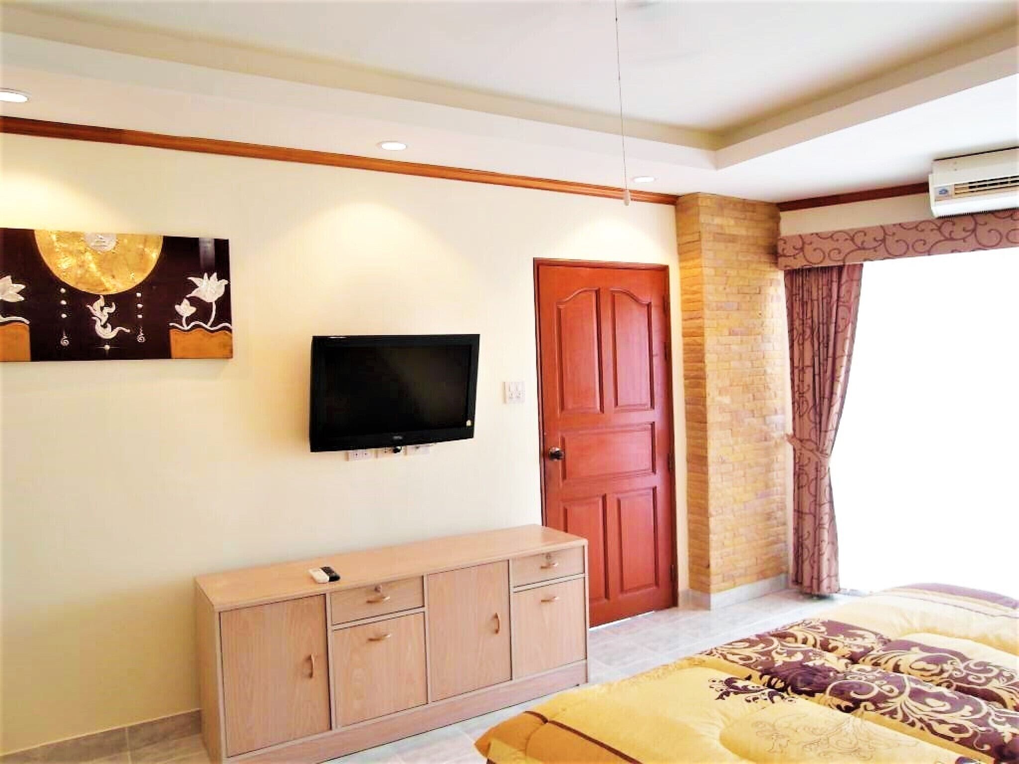 A bedroom with a bed, a TV mounted on the wall, a wooden cabinet, and a door.