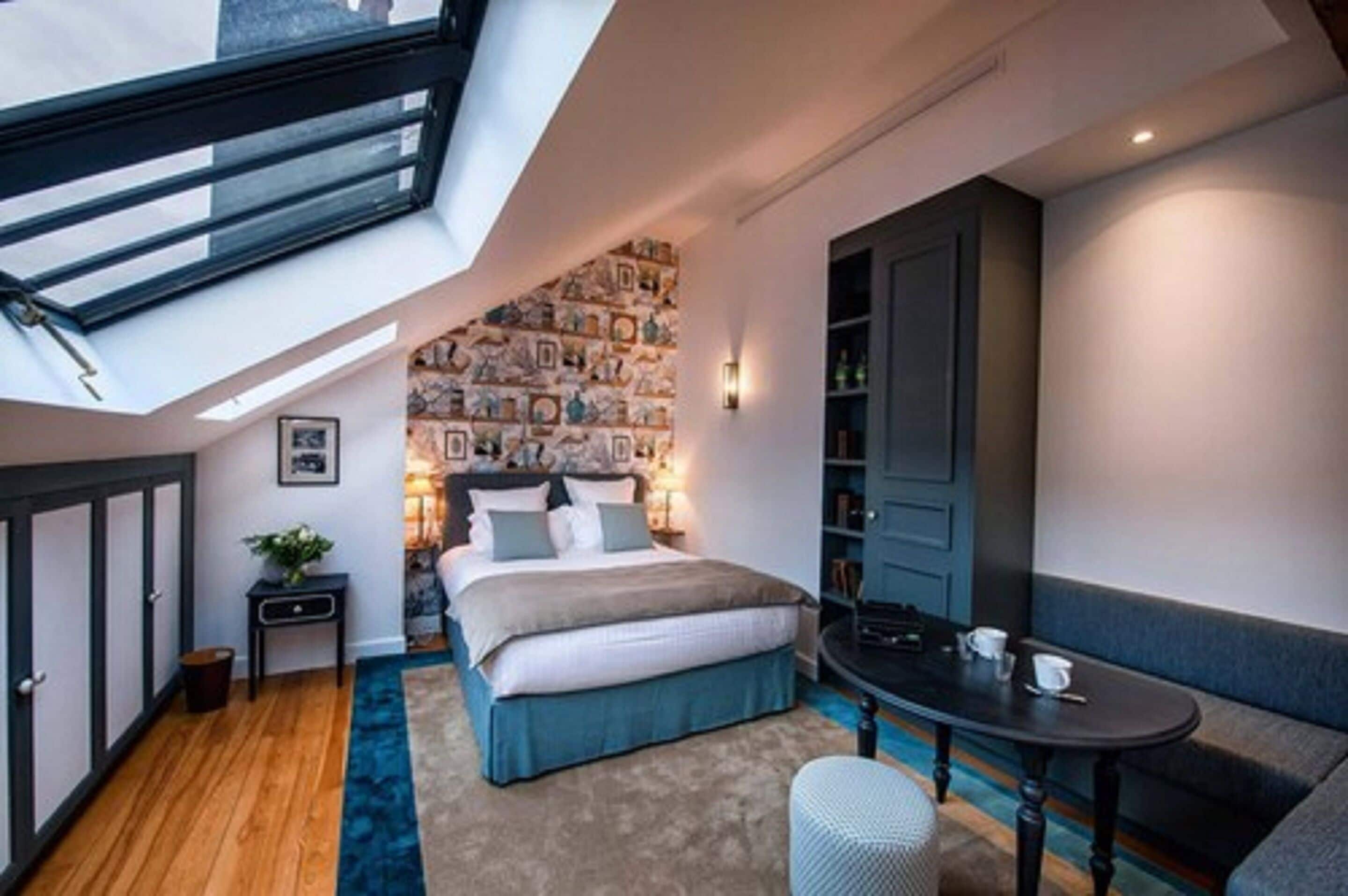 A compact bedroom with a skylight, a bed, a small table, and a seating area.