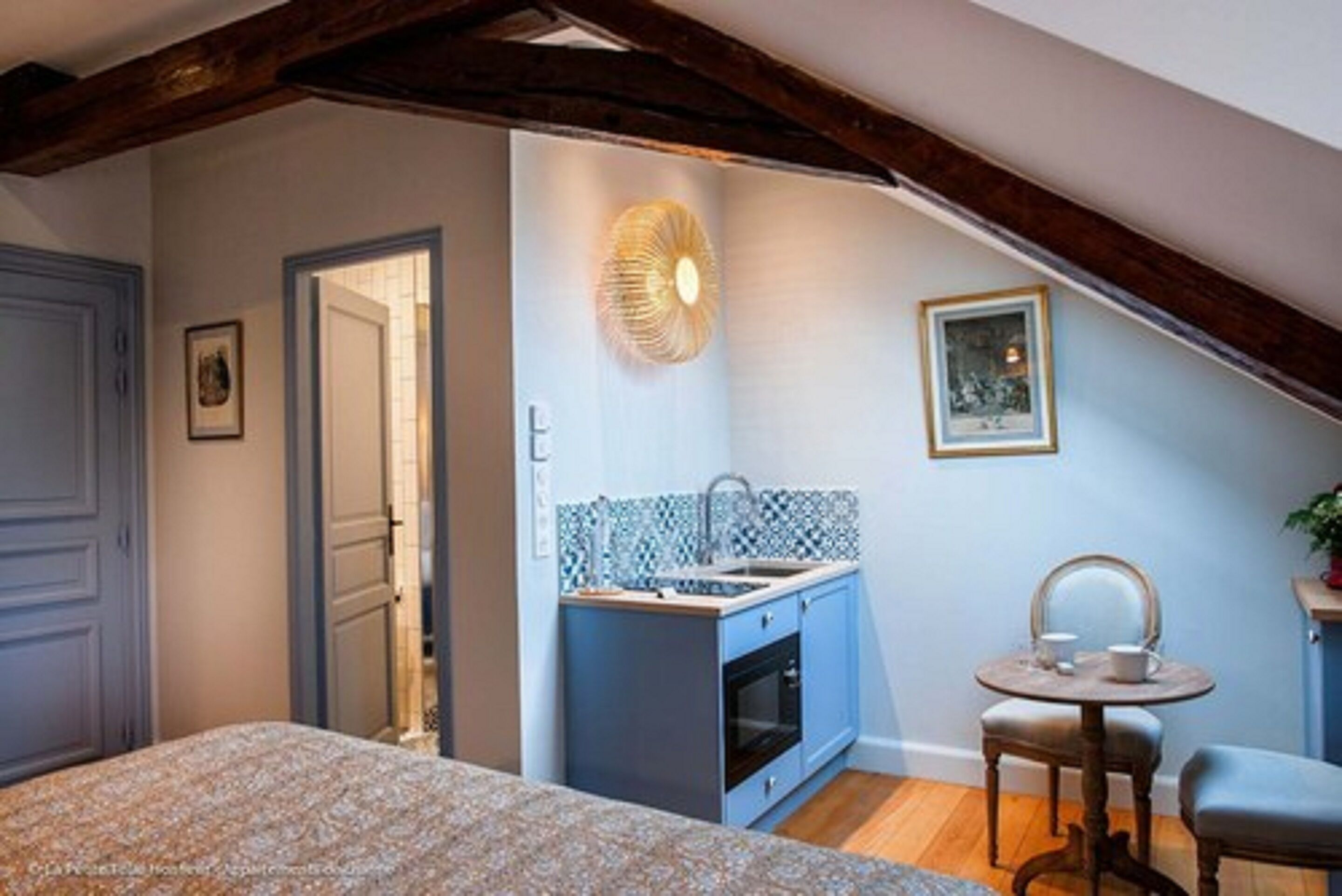 A compact room with a bed, a small kitchenette, a dining table with chairs, and a ceiling fan.