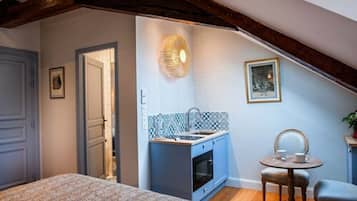 Ein kleines Zimmer mit Bett, einer kleinen Küchenzeile, einem Esstisch mit Stühlen und einem Deckenventilator.
