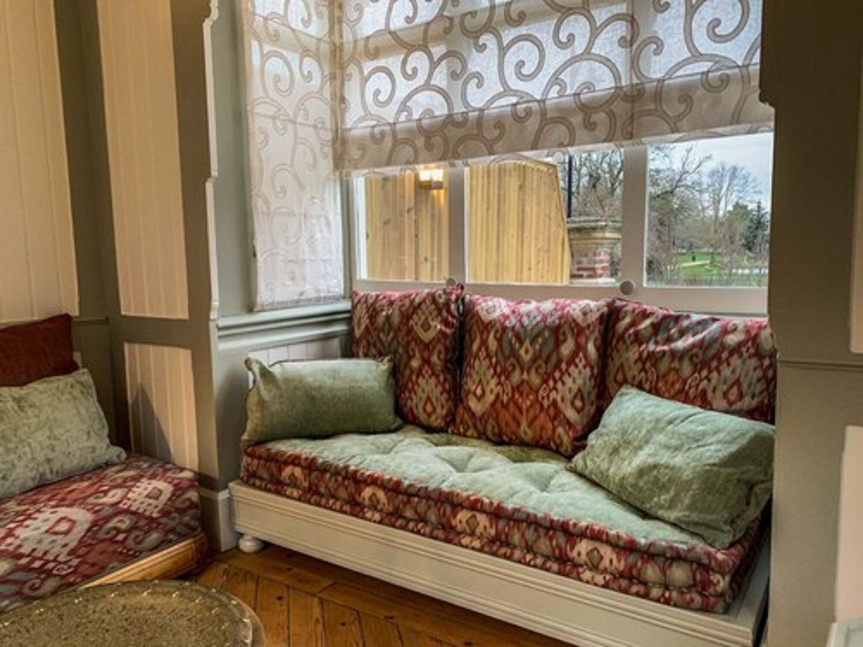 A cozy room with a patterned sofa, a cushioned bench, and a large window with curtains.