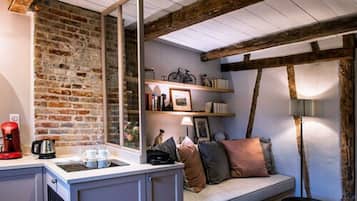 A cozy room with exposed wooden beams, a brick wall, a sofa with cushions, a coffee machine, and a lamp.