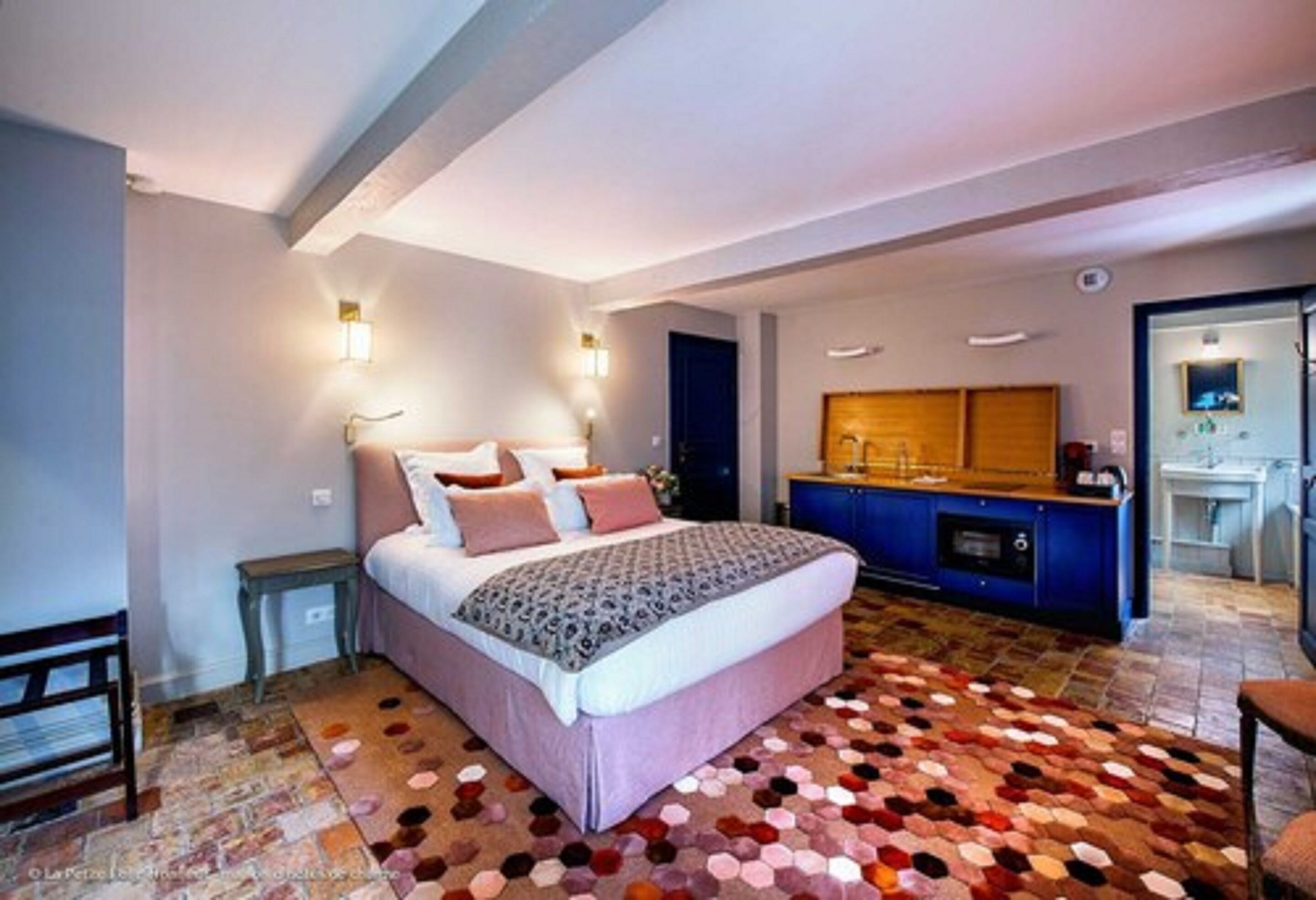 A bedroom with a large bed, a small bedside table, a dresser, and a bathroom visible through an open door.