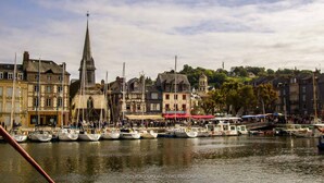 A harbor with boats docked, historic buildings, and a prominent church steeple. - La Petite Folie (Honfleur)