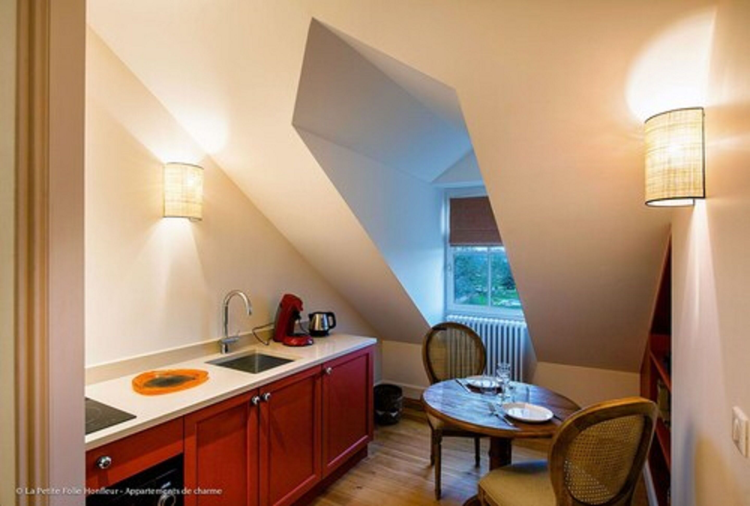 A compact kitchen with a red countertop, a sink, and a window providing natural light.
